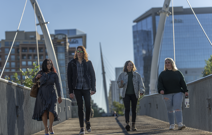 four students walking across urban bridge on sunny day