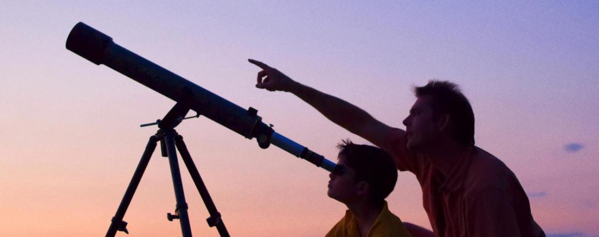 一个大人和一个孩子在日落时通过望远镜观看. 成年企鹅指着天空.